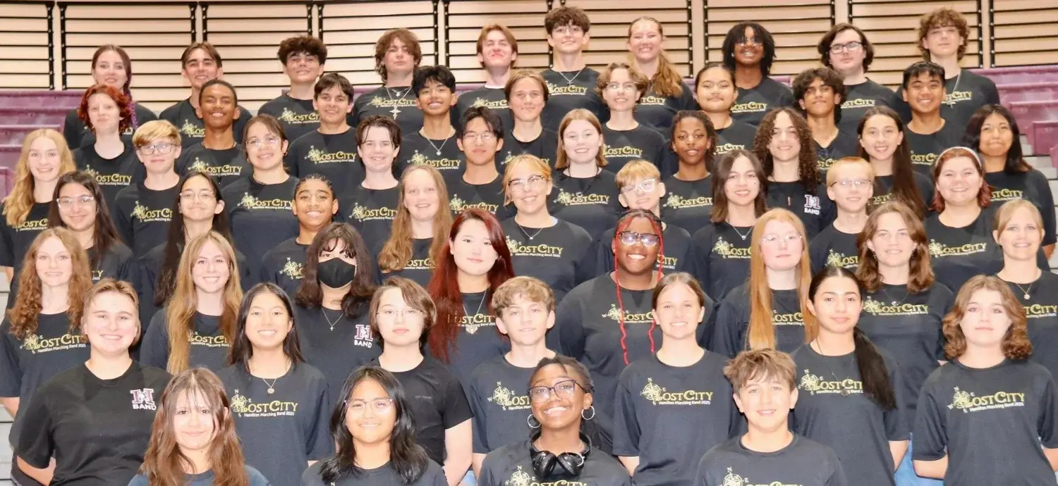 The 2025 Hamilton Marching Band in matching Lost City shirts, smiling in the bleachers